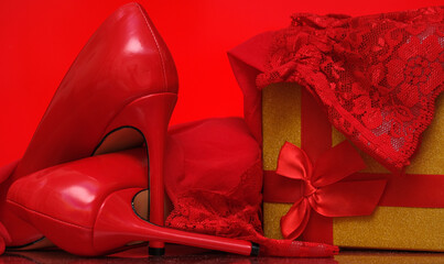 red stiletto heels and red stockings and gold gift box on red background