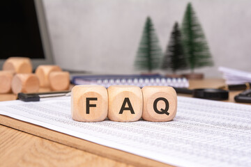 Wooden Blocks Displaying Frequently Asked Questions on Desk Surrounded by Office Supplies