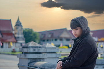 Portrait of young asian boy who has broken family, homeless, living, sitting and standing in front of Buddhist temple, sunlight edited, concept for social problems of young people around the world.