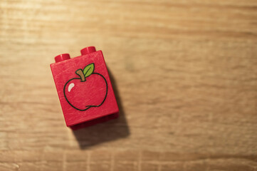 Obraz premium Red Lego Duplo block with an apple icon on a wooden table
