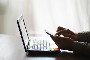 Hands using laptop and phone for online shopping, close up clean image in front of the window in soft light