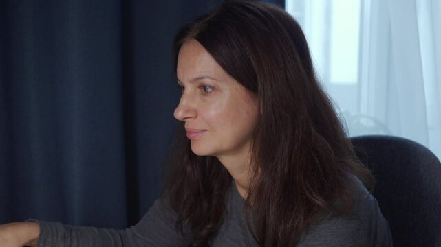 woman working on computer on table at home. Female face attentively reading something on laptop screen. Woman talking, smiling, laughing.