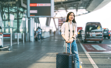 Standing tourist woman with travel luggage waiting at bus terminal for transport on day