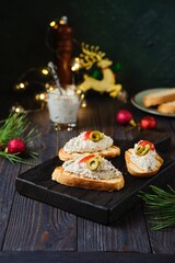 Cold appetizer, mackerel rillettes on white bread toasts on wooden board in Christmas decor on dark wooden background. Holiday appetizers. Recipes fish.