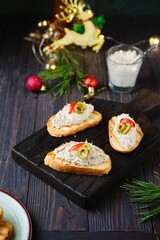 Cold appetizer, mackerel rillettes on white bread toasts on wooden board in Christmas decor on dark wooden background. Holiday appetizers. Recipes fish.