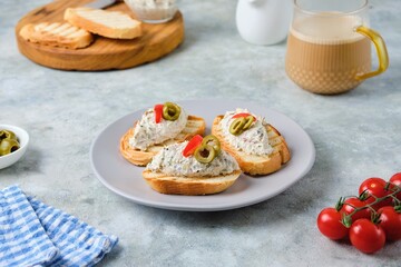 Cold appetizer, mackerel rillettes on white bread toasts on ceramic plate on gray concrete background. Recipes fish, seafood.