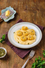 Side dish or main course, pumpkin gnocchi in the shape of a pumpkin made of potatoes and pumpkin puree with cream sauce on a ceramic plate on a brown wooden background.