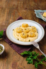 Side dish or main course, pumpkin gnocchi in the shape of a pumpkin made of potatoes and pumpkin puree with cream sauce on a ceramic plate on a brown wooden background.