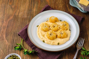 Side dish or main course, pumpkin gnocchi in the shape of a pumpkin made of potatoes and pumpkin puree with cream sauce on a ceramic plate on a brown wooden background.