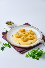 Side dish or main course, pumpkin gnocchi in the shape of a pumpkin made of potatoes and pumpkin puree with cream sauce on a ceramic plate on a white plastic background.
