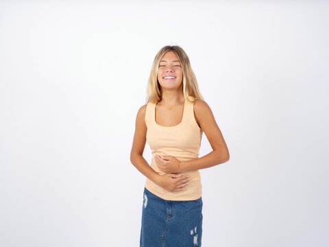 Beautiful teen girl wearing sleeveless t-shirt smiling and laughing hard out loud because funny crazy joke with hands on body.