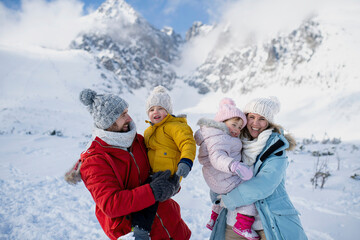 Young family is enjoying winter holiday in the mountains, standing in the middle of snowy landscape.
