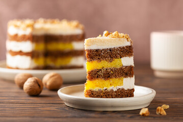 Piece of vegan pumpkin or carrot layered cake with coconut cream, nuts and orange confit with cup of tea. Sugar, gluten and lactose free.