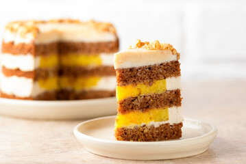 Piece of vegan pumpkin or carrot layered cake with coconut cream and orange confit on a light background. Sugar, gluten and lactose free.