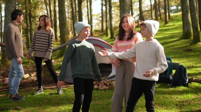 Caucasian sister and brothers talking standing in a green forest while camping with their parents