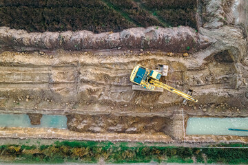 an excavator digging a trench at a construction site, overhead view from a drone, background for...