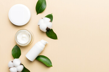 Organic cosmetic products with cotton flower and green leaves on color background. Copy space, flat lay