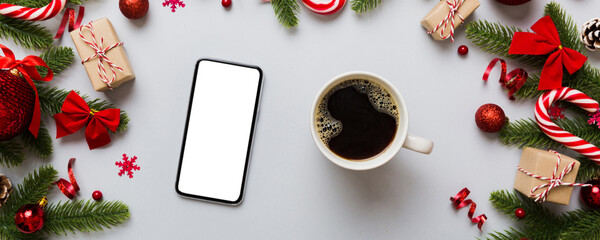 top view of smart phone with hot cup of coffee. Christmas decoration on colored background