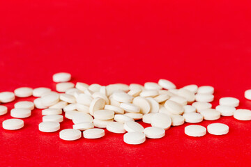 Heap of white pills on colored background. Tablets scattered on a table. Pile of red soft gelatin capsule. Vitamins and dietary supplements concept