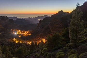 Mountain valley at dusk with glowing village lights.