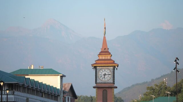 A Close shot of clock tower at Lal chowk surrounded by houses or building with a view of towering snow capped Himalaya mountains visible in the background, Srinagar, Jammu and Kashmir, India