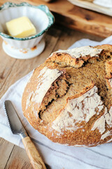 Loaf of freshly baked bread resting on a kitchen towel with butter and bread knife