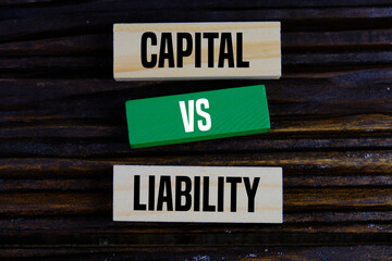 color wooden block with text of CAPITAL VS LIABILITY as an economy and financial concept on dark background.