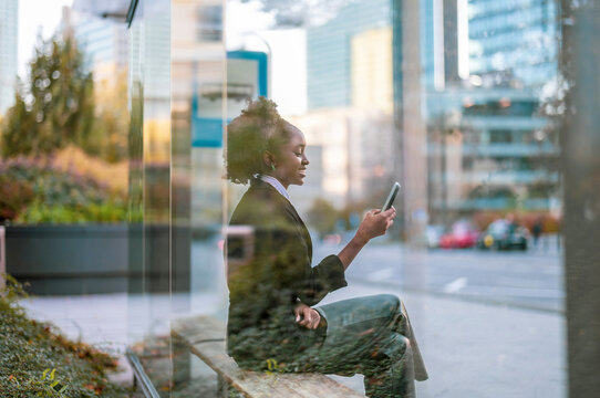 Young woman using smart phone at the bus stop in the city