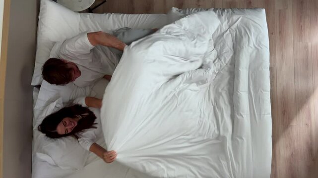 A happy young couple in their cozy bedroom, smiling and relaxing together in a warm ambiance before sleep. A peaceful and harmonious bedtime routine for two young adults. Happy couple in love to bed