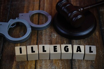 Judge gavel, handcuffs, on wooden table with text of ILLEGAL as a legal concept