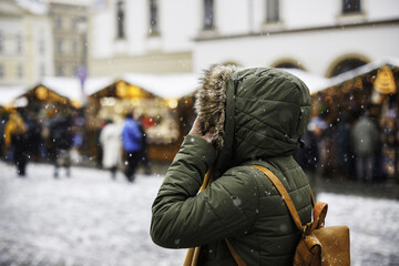 Woman is walking to Christmas market on town square during the Advent holiday. Snowing in city at...