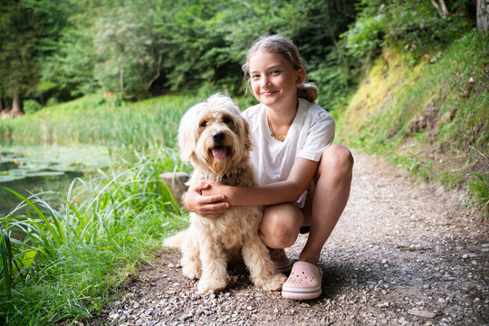 Smiling girl crouching with golden doodle dog in forest