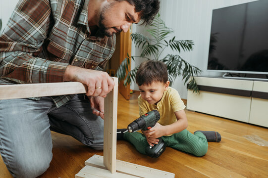 Father with son using drill and assembling furniture at home