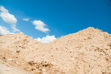 a mountain of sand against a blue sky and clouds