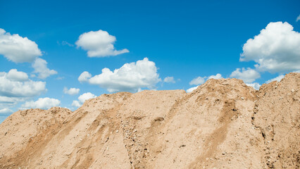 a mountain of sand against a blue sky and clouds