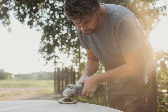 Mature man polishing wooden table in back yard