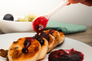 Female hand with spoon with jam preparing cheese pie. Delicious snack with cheesecake and homemade Blueberry jam