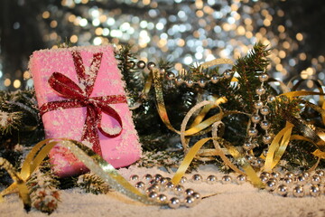 Christmas background with a pink gift on the background of a snow-covered green fir tree on a shiny background