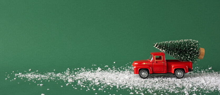A charming vintage red toy truck carries a miniature Christmas tree across a snowy path. The green background enhances the festive and nostalgic feel of this holiday-themed image
