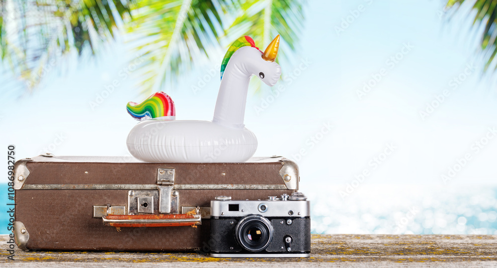 Poster a bag with travel stuff, camera, and floating flamingo placed on a table
