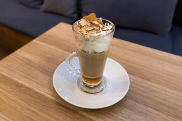 A transparent cup of gingerbread latte showcases the drinks layered texture: rich coffee at the bottom and delicate foam on top. The foam is sprinkled with cinnamon, evoking a cozy winter atmosphere.