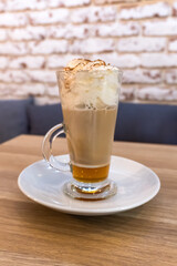 Gingerbread latte in a transparent glass cup. The creamy foam is topped with hints of cinnamon and grated nutmeg. Reflecting warm light, the drink evokes a sense of festive coziness, winter evenings.