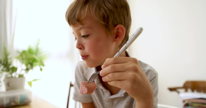 Young boy attempts to eat sausage meal using only a fork distracted and looking at the table carefully