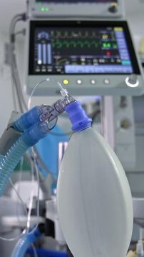 Inflating ambu bag hanging in the surgery room. Screen with life signs from a lung ventilator machine at backdrop in blur. Vertical video