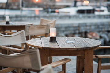 Enjoy a serene evening at a waterfront location with wooden tables, cozy chairs, and candles casting a warm glow as day turns to night