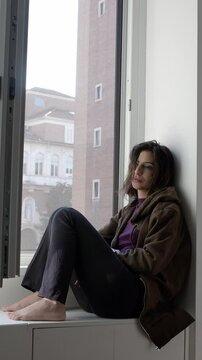Vertical: A young girl sits alone by the window, feeling sad and lonely, reflecting on her emotions and the quiet around her.