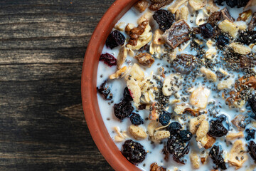 Whole grain oat muesli with dried fruits, nuts, raisins, berries and almond milk in clay bowl on wooden table, top view, closeup. Background of organic muesli for breakfast
