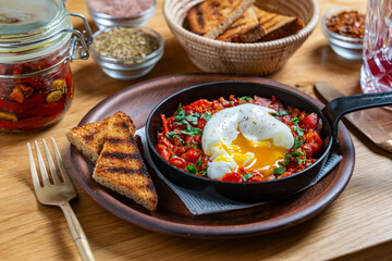 Delicious shakshuka in frying pan for breakfast, closeup. Homemade shakshuka from poached egg, onion, bell pepper, red tomato and green parsley