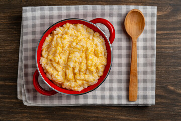 Sweet pumpkin porridge with rice, honey and milk in a red saucepan on a wooden table, closeup, top view. Autumn comfort breakfast food