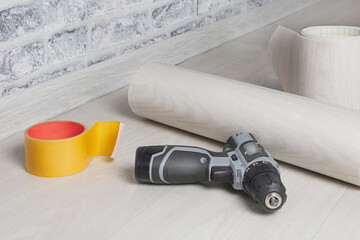 There is a roll of linoleum on the floor, an electric screwdriver and construction tape....